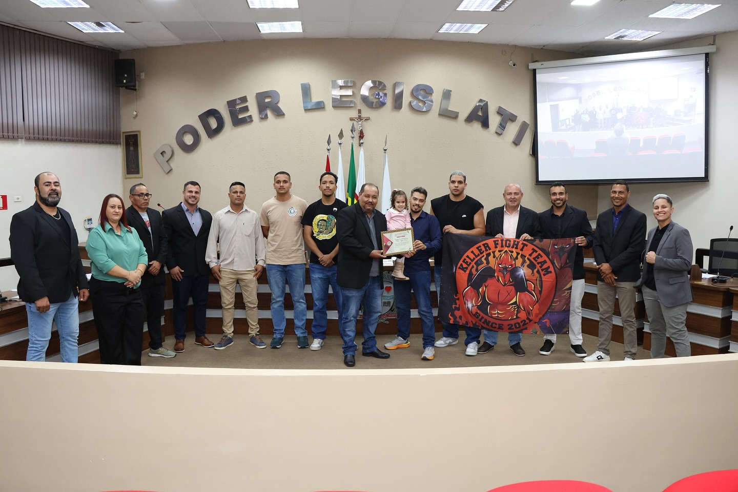 Equipe da Keller Fight Team no plenário da Câmara Municipal de Rafard, segurando a bandeira e o diploma da Moção de Aplauso.